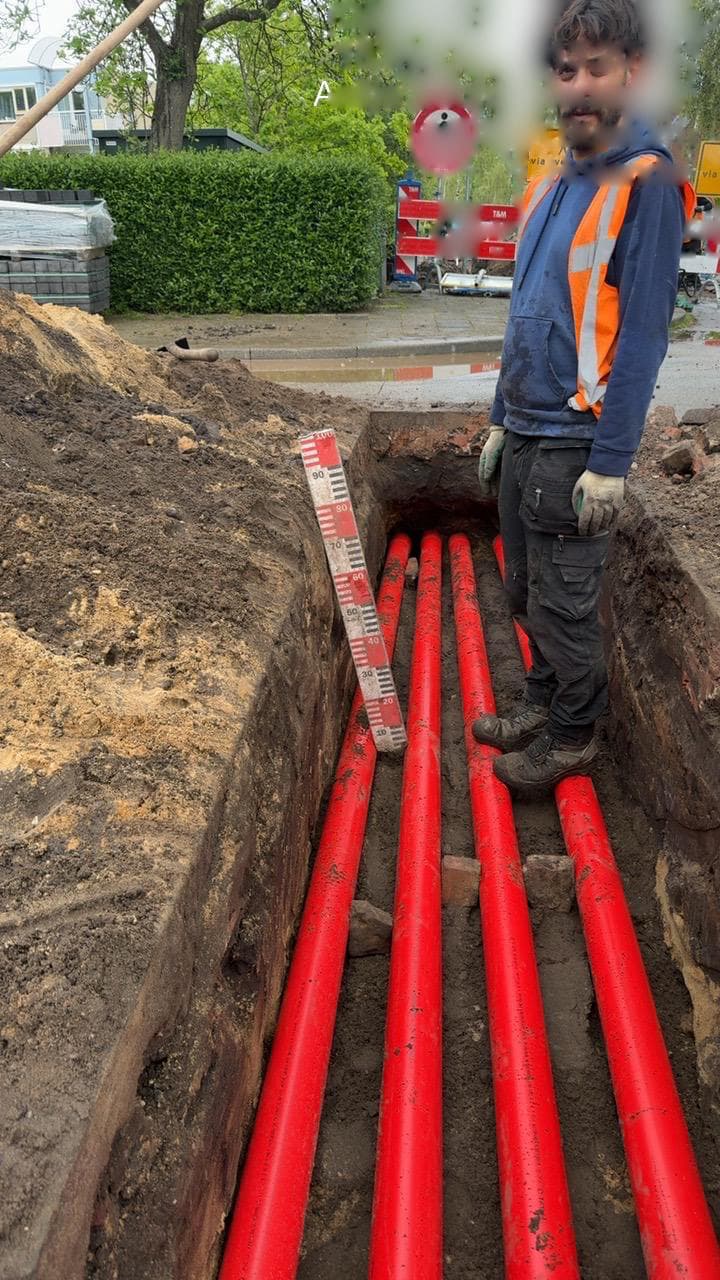 Kabelaanleg met rode leidingen in een sleuf tijdens infrawerk